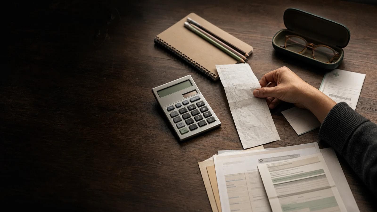 Mesa con calculadora, cuaderno, comprobantes y antecedentes de gastos escolares y médicos.